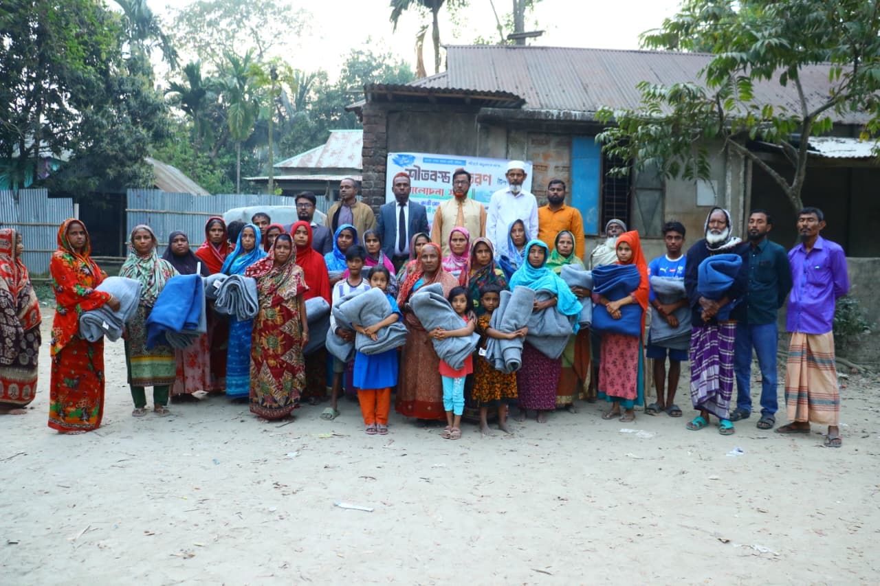 খোলা উঠোনে নারী, পুরুষ ও শিশুরা কম্বল হাতে একসঙ্গে দাঁড়িয়ে আছেন।