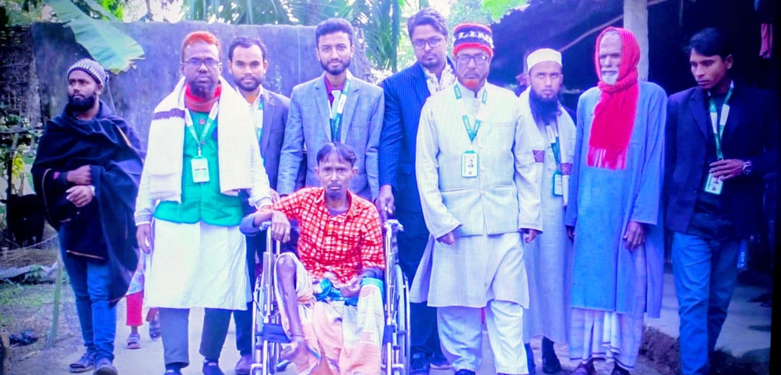 একজন হুইলচেয়ার ব্যবহারকারীকে ঘিরে খোলা জায়গায় কয়েকজন দাঁড়িয়ে আছেন।