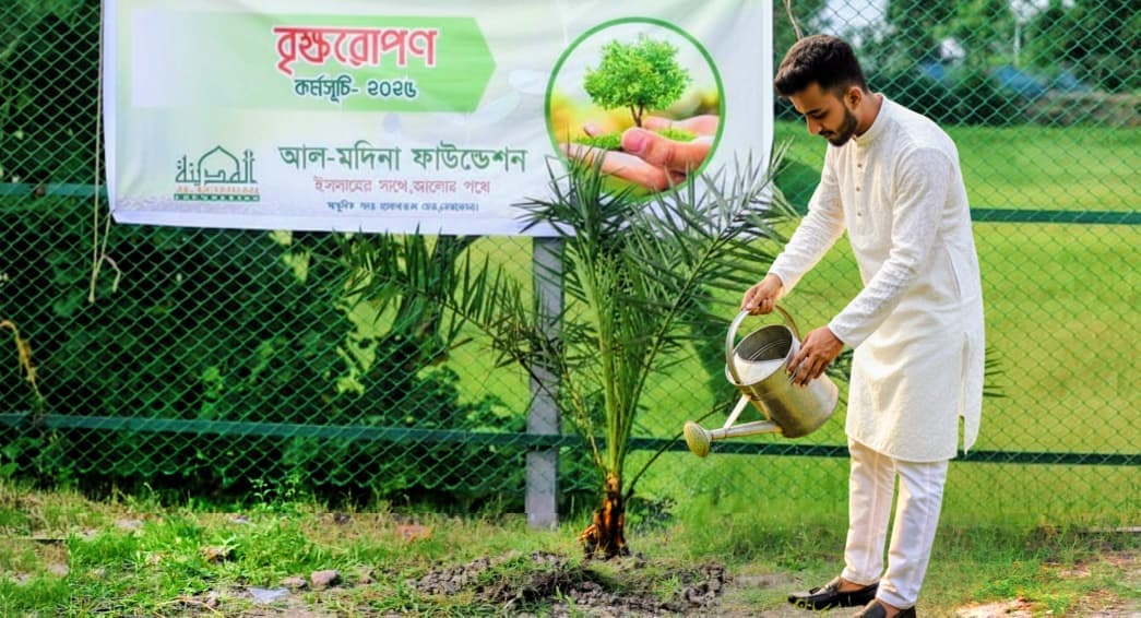 বৃক্ষরোপণের ব্যানারের সামনে একজন ছোট গাছের গোড়ায় পানি দিচ্ছেন।
