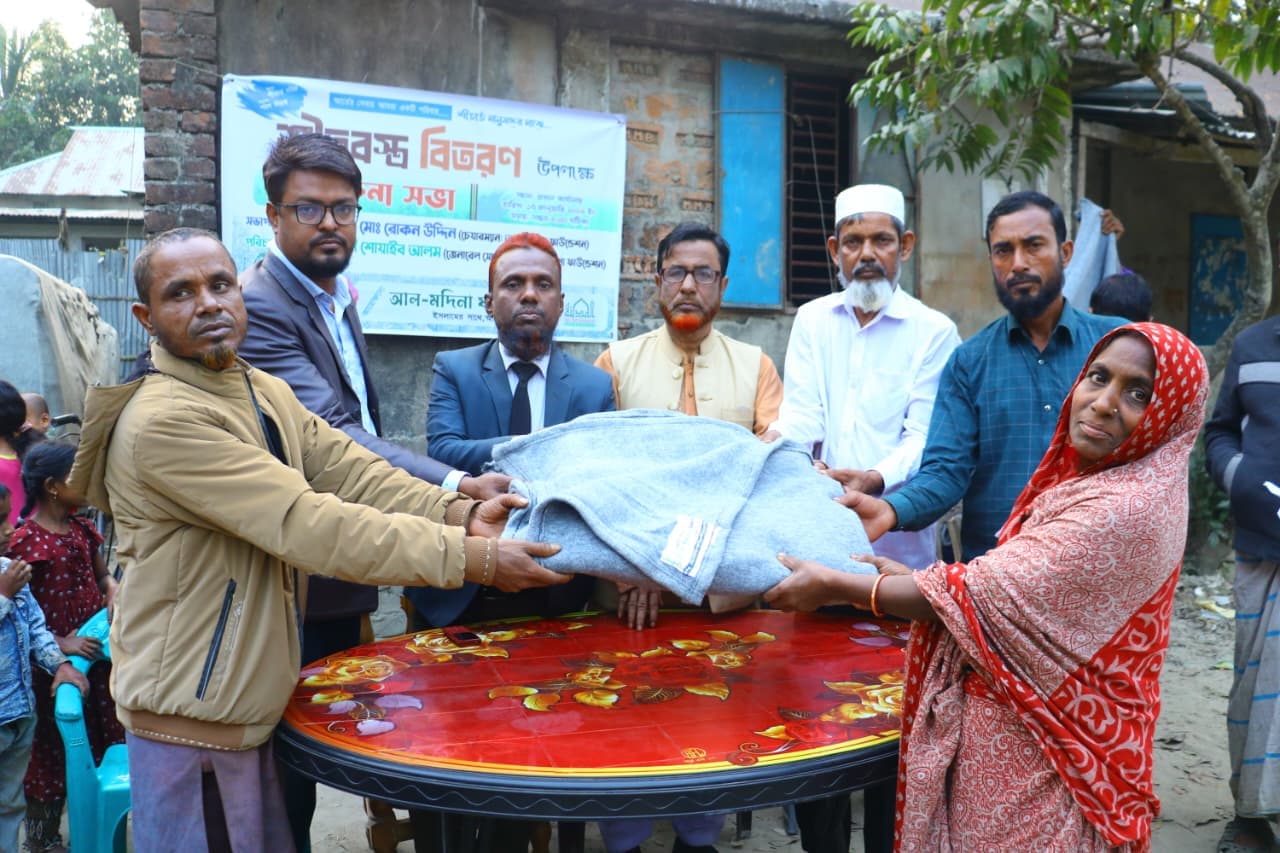 লাল ছাপার ওড়না পরা একজন নারী টেবিলের পাশে ধূসর কম্বল নিচ্ছেন।