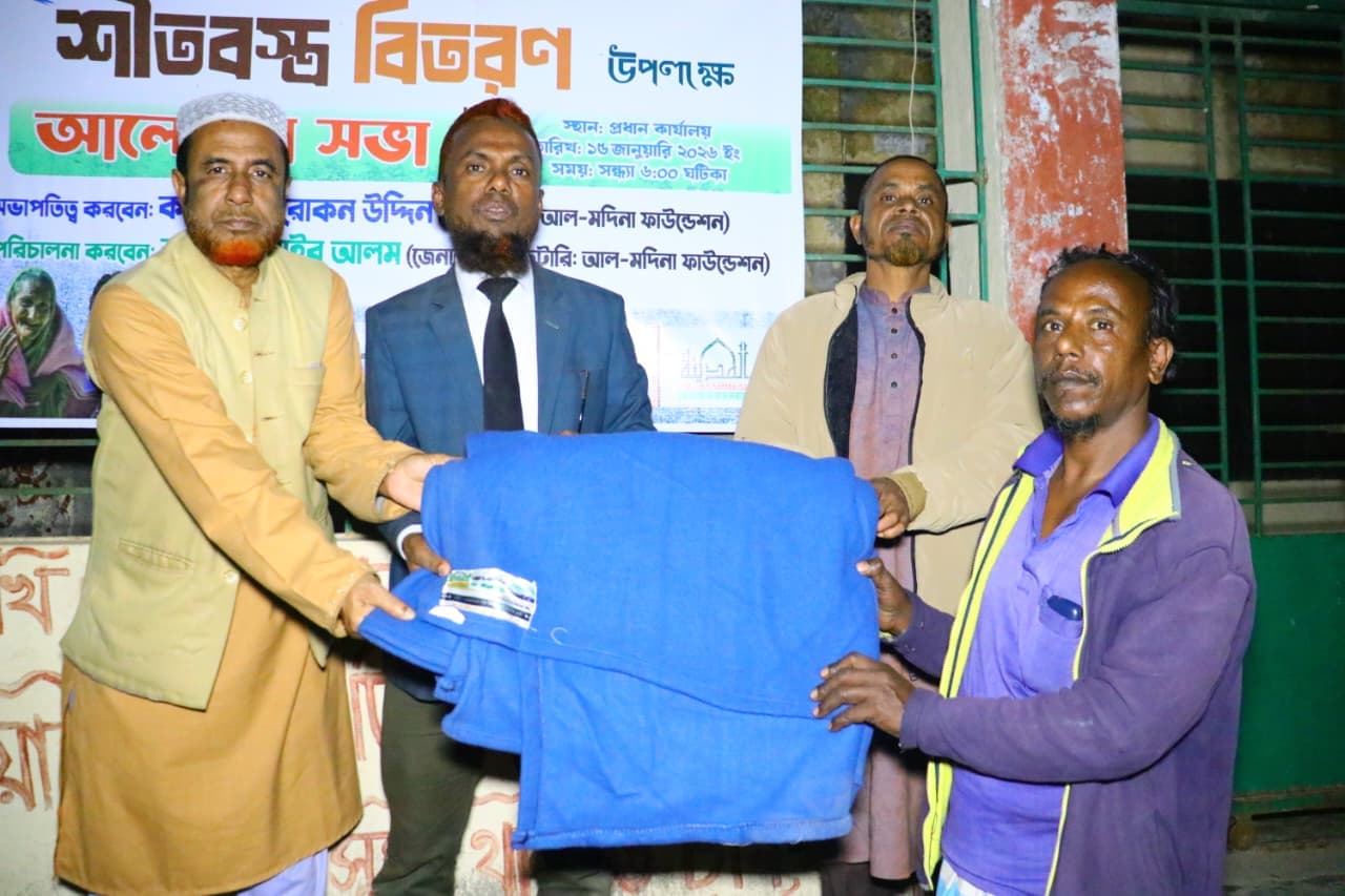 বেগুনি জ্যাকেট পরা একজন পুরুষ ভবনের সামনে নীল কম্বল নিচ্ছেন।