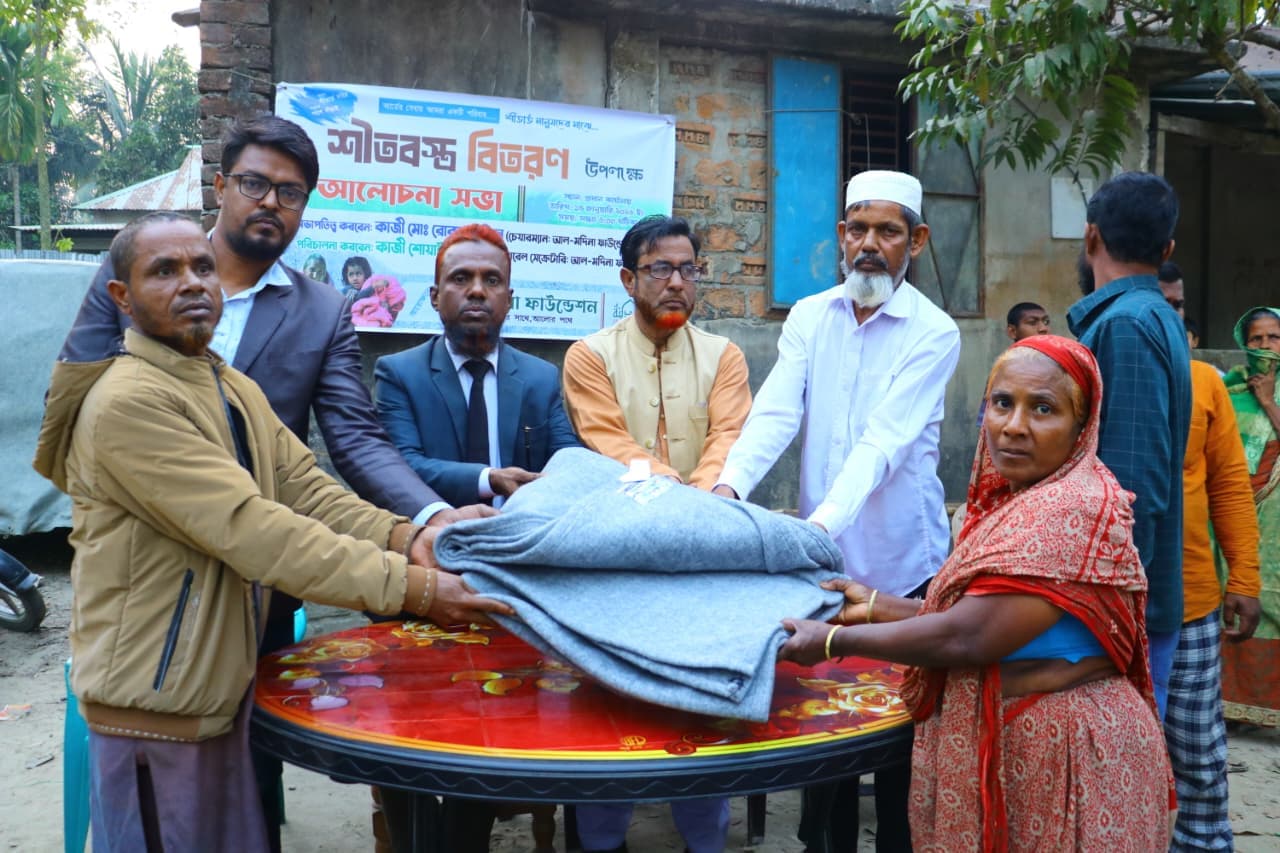 খোলা উঠোনে একজন নারীকে ভাঁজ করা ধূসর কম্বল দেওয়া হচ্ছে।